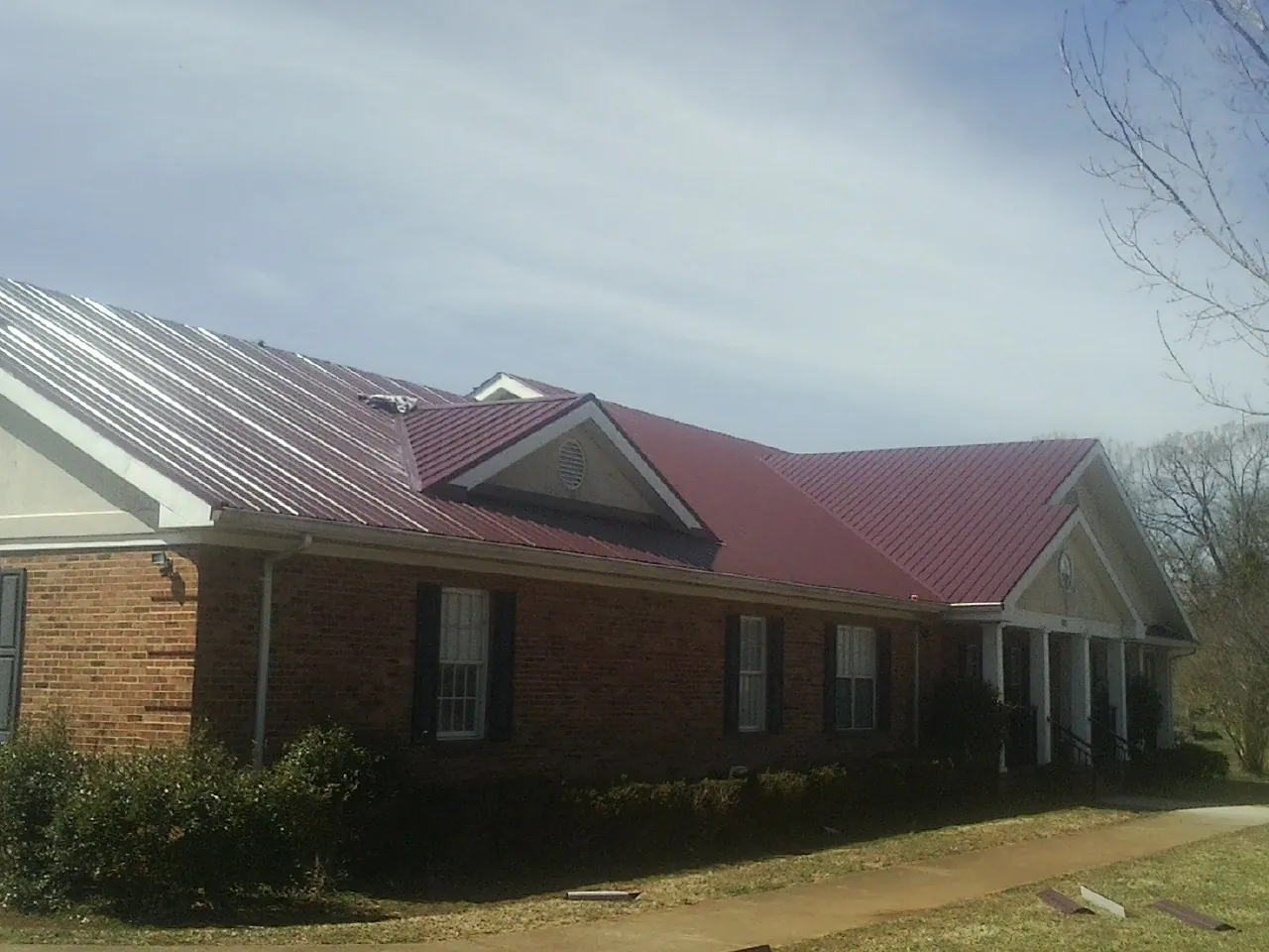 Red metal roof with gabled entries on a long brick building, from a Hail Damage Roof Repair job in Oneida